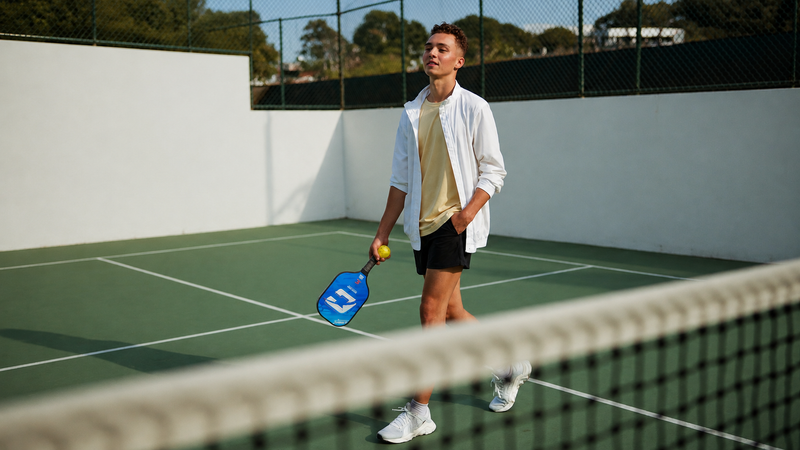 Player walking on a tennis court holding a blue CIPTON pickleball paddle