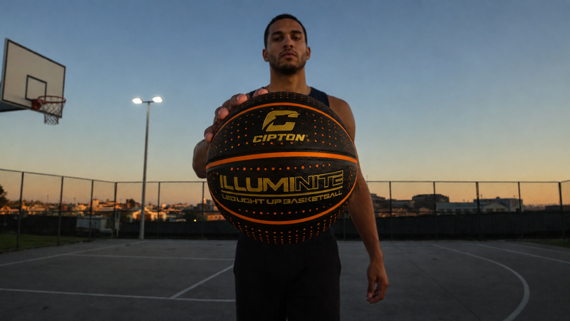 Player holding the CIPTON Illuminite LED basketball on an outdoor court at dusk